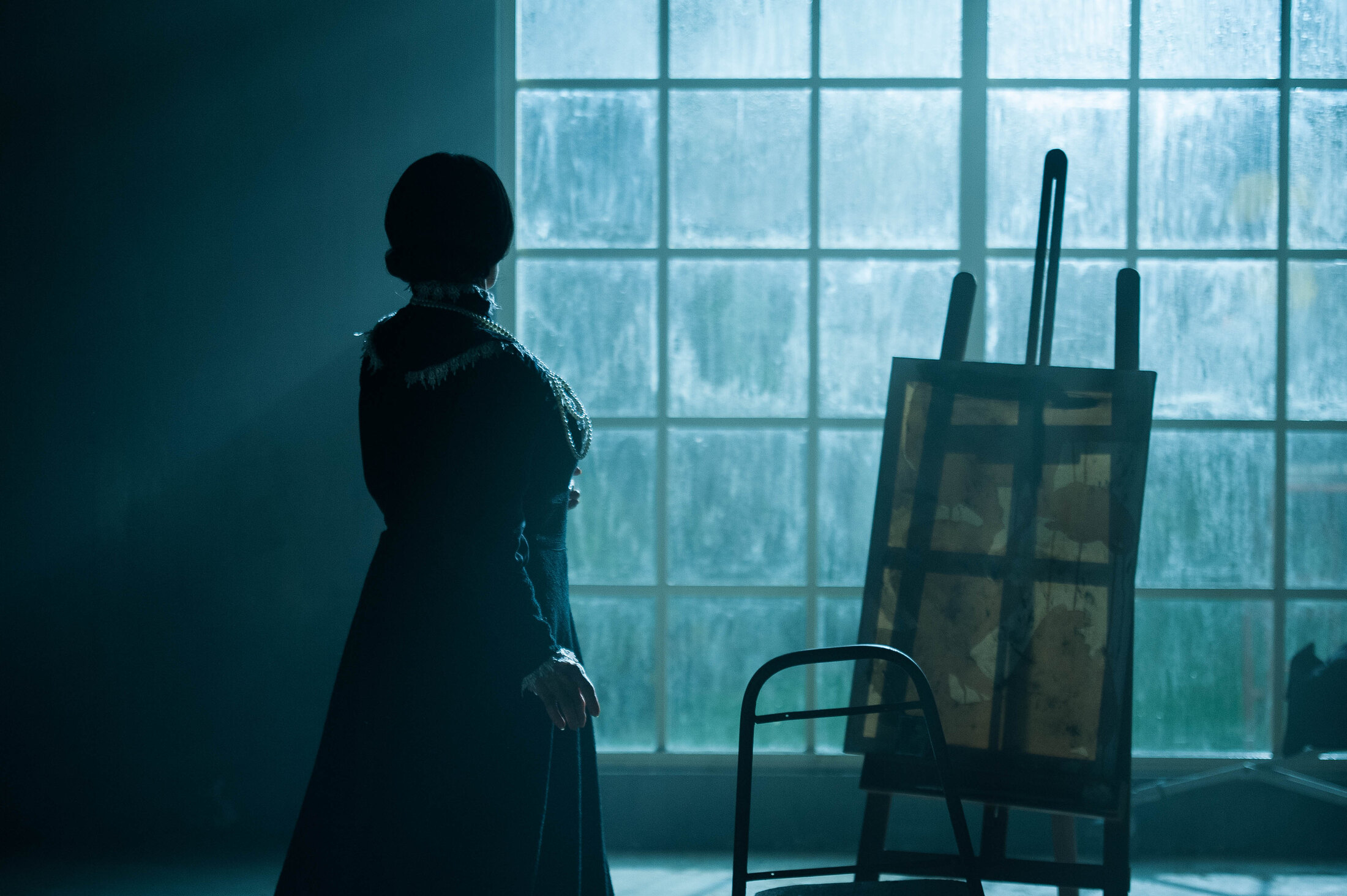 Performer beside an easel in blue window light on the Kintsugi set