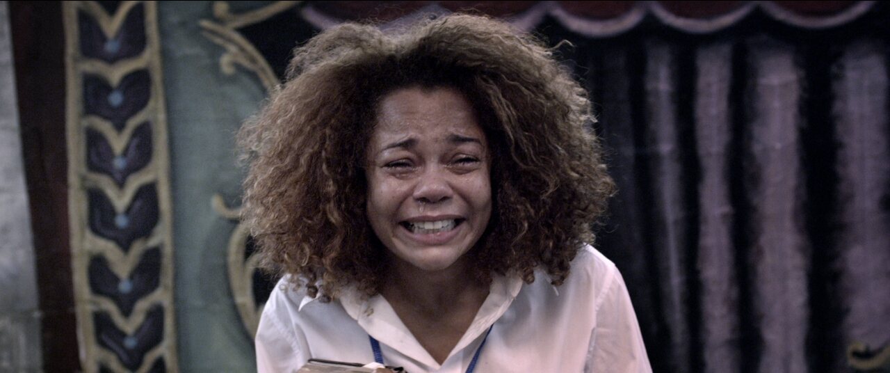 Film still: a young woman breaking down in front of a painted circus curtain